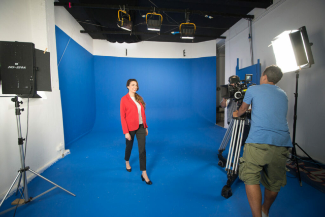 Instudio.org: Model in Red Jacket walking in Studio C Blue Screen with Camera Operator and lights